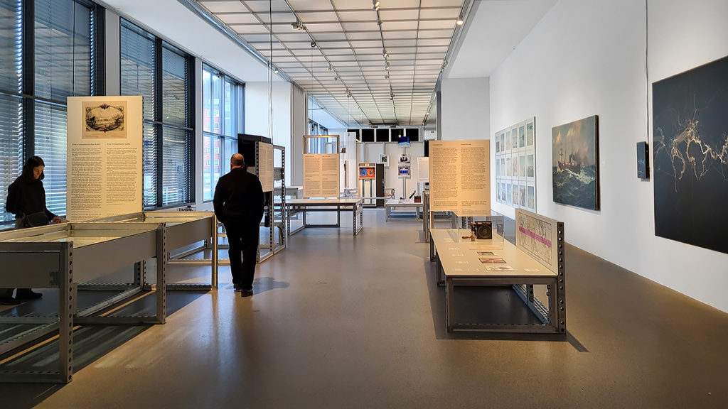 Besucher:innen und Ausstellungsstücke der Ausstellung "City in the Cloud: Data on the Ground. The Architecture of Data" im Architekturmuseum in der Pinakothek der Moderne in München